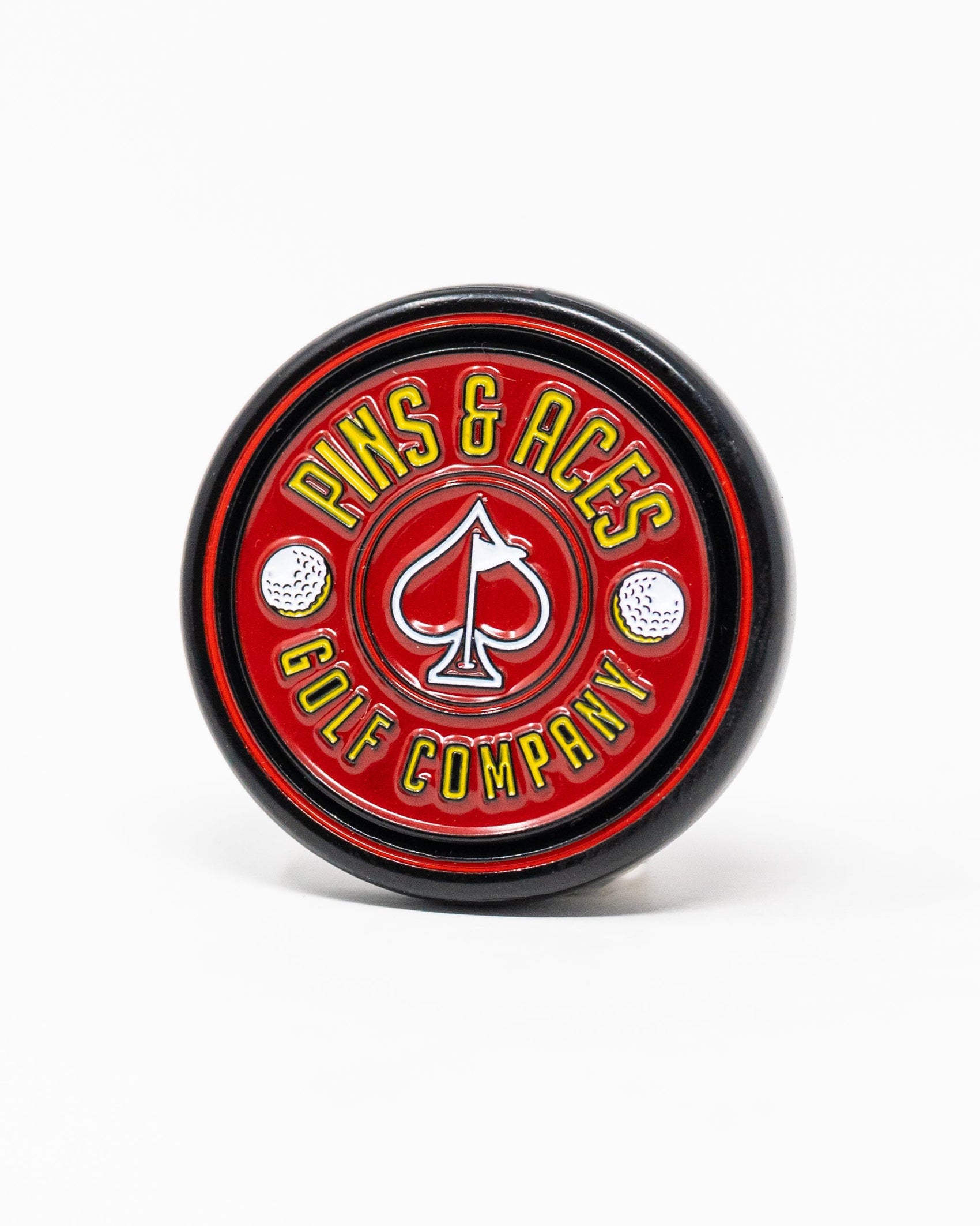 The Pop Out Medallion Ball Marker - Red by Pins and Aces features a round, red design with a white spade and "Pins and Aces" text, bordered by golf balls on a white background.