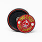 The Pop Out Medallion Ball Marker - Red by Pins and Aces features a round red marker with “Pins & Aces Golf Company” around an ace of spades and golf balls, displayed next to its black magnetic holder.