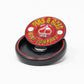 The Pop Out Medallion Ball Marker - Red by Pins and Aces features a round, red design with company text and an ace of spades symbol, shown upright in a black circular case against a white background.
