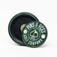 The Pop Out Medallion Ball Marker - Green by Pins and Aces is a round green and black magnetic golf accessory, featuring "Pins and Aces" with an illustrated spade, shown upright with its magnetic back displayed flat behind it.