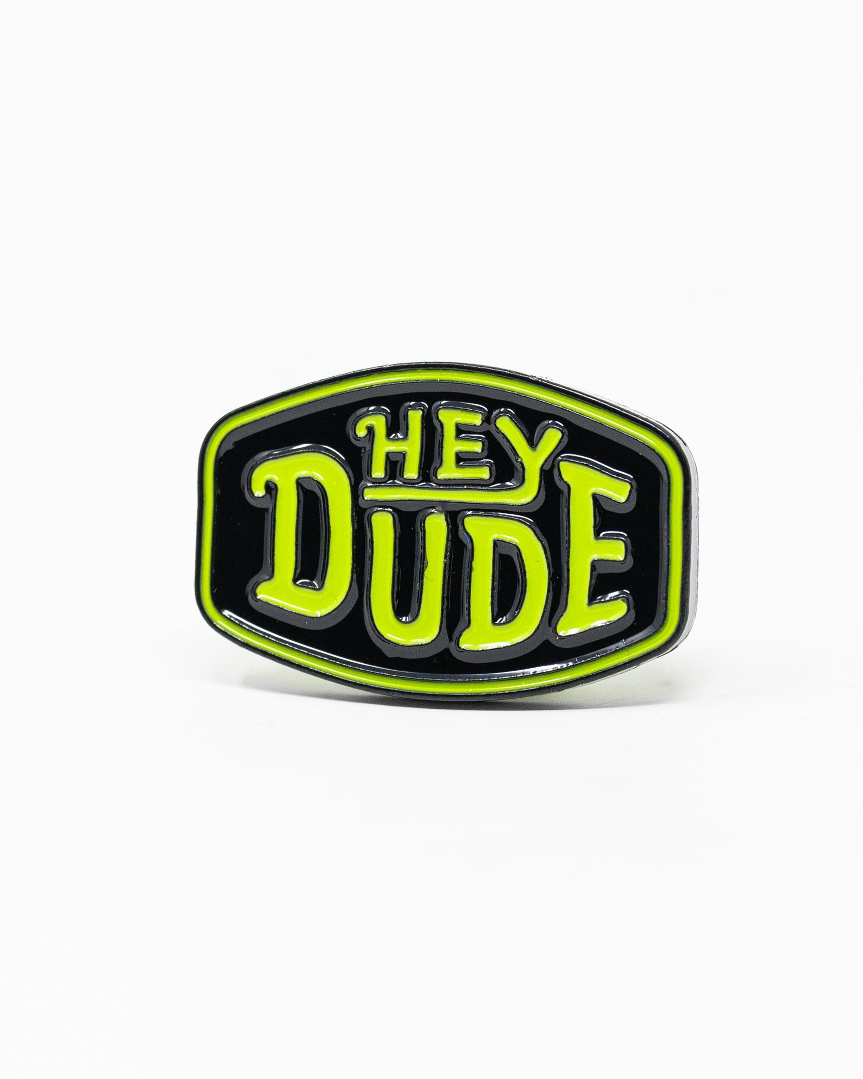 The Pins and Aces HEYDUDE - Logo Ball Marker is a black enamel pin that doubles as a cast metal ball marker, displaying HEY DUDE in bold yellow-green letters with white trim on a simple white background.