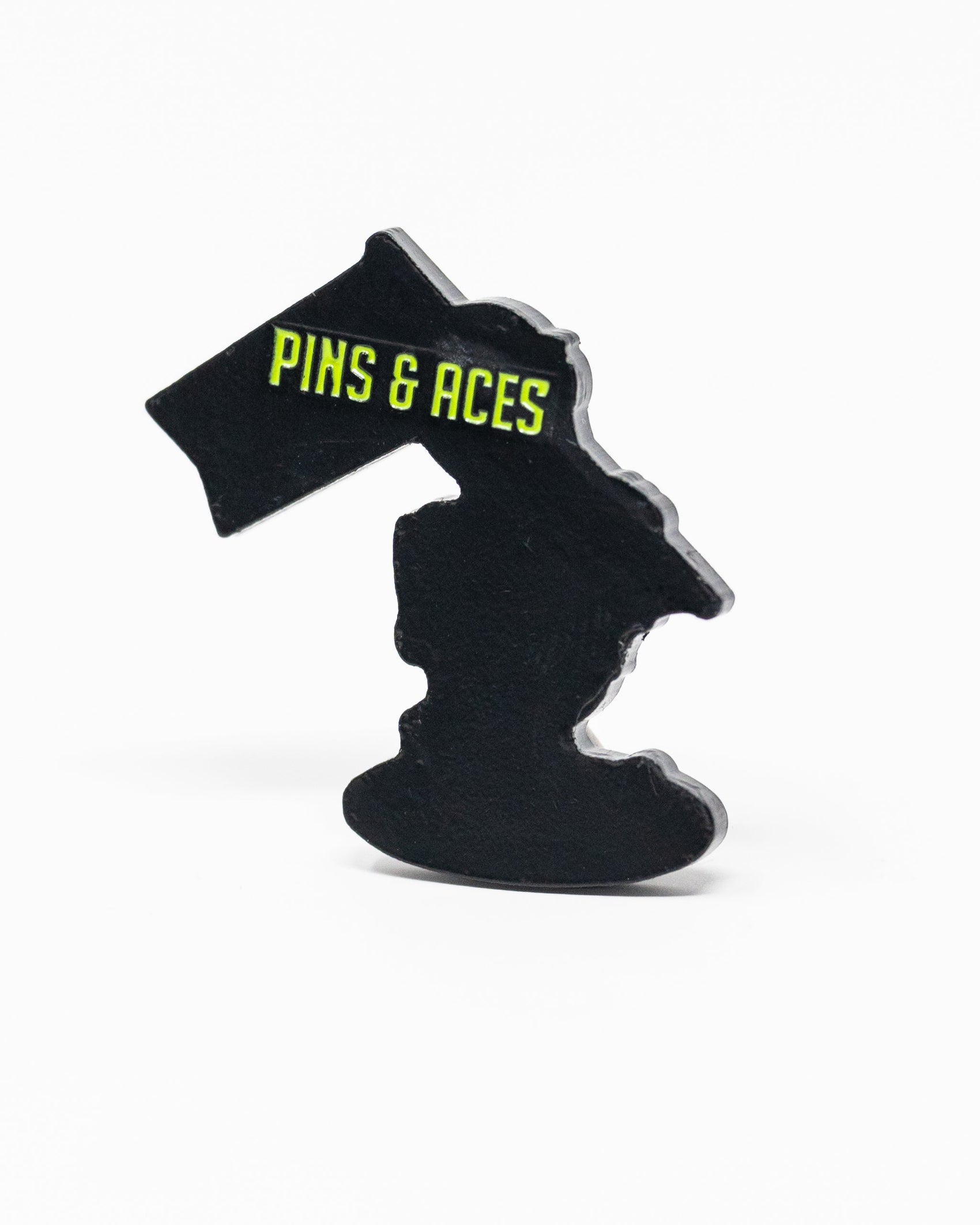 A black enamel HEYDUDE - Alien Ball Marker by Pins and Aces, shaped like Michigan, features bold yellow branding on a flag and is photographed against a plain white background.