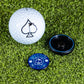 The Pins and Aces Pop Out Medallion Ball Marker - Navy, featuring a spade symbol and navy design, and a black magnetic holder are displayed on green artificial turf.