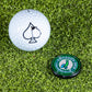 A white golf ball with a black spade and a round green Pop Out Medallion Ball Marker - Crooked Dick by Pins and Aces, featuring a bird logo, rest on green artificial turf.
