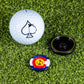 The Pins and Aces Pop Out Medallion Ball Marker - Colorado, featuring a spade and Colorado flag, comes with a black magnetic holder and golf ball, all displayed on green artificial turf.
