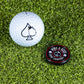 A Pop Out Medallion Ball Marker - Black by Pins and Aces with a spade logo lies on artificial grass beside a golf ball marked with a black spade.