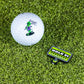 A golf ball with a green alien holding a flag that says "TAKE ME TO YOUR GOLF COURSE," paired with the Pins and Aces HEYDUDE - Hole 51 Ball Marker, which reads: WARNING: HOLES! NO TRESPASSING, set on artificial grass.