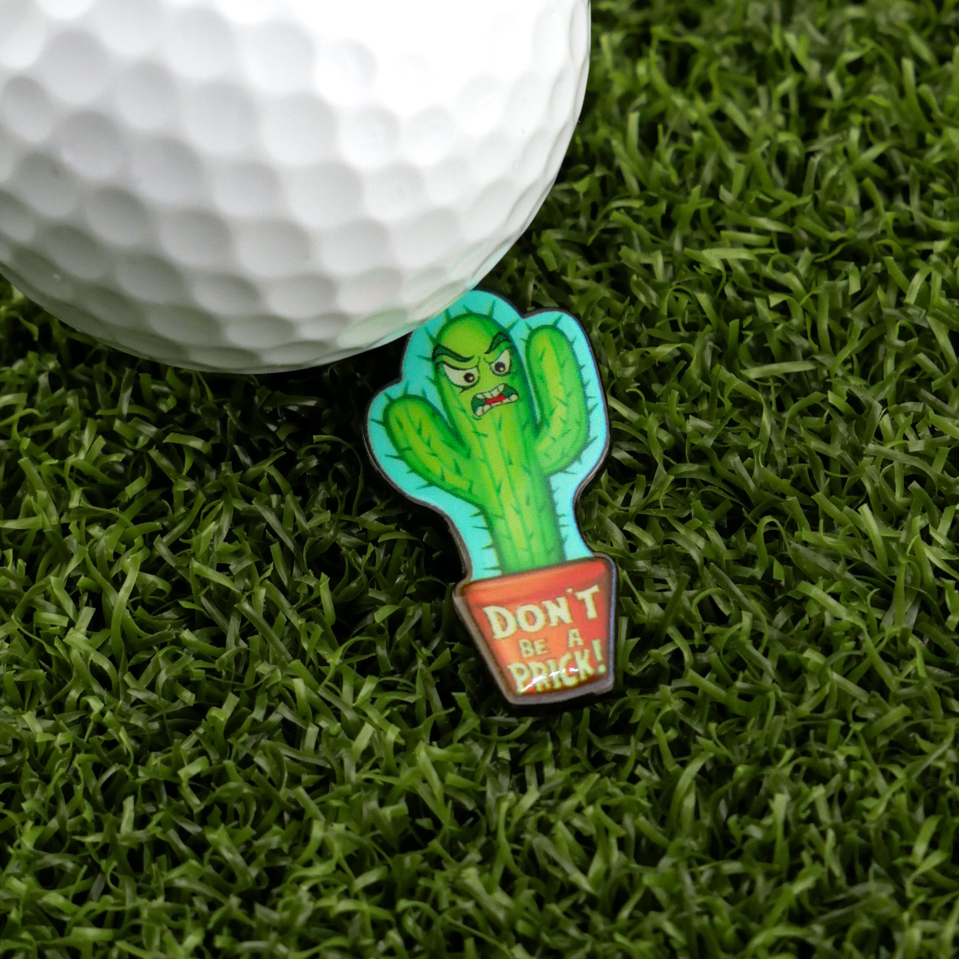 The Don’t be a Prick golf ball marker by Logie Joe's Golf features an angry cactus pin in a pot inscribed “DONT BE A PRICK!”—a premium, quirky accessory for standout golfers.