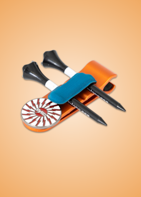 Two black golf tees and a striped round ball marker rest on the orange THE BYRD GOLF CLYP - Orange Oriole by The Byrd, LLC, secured with a blue strap. The gradient orange backdrop is perfect for organizing your golf accessories in style.