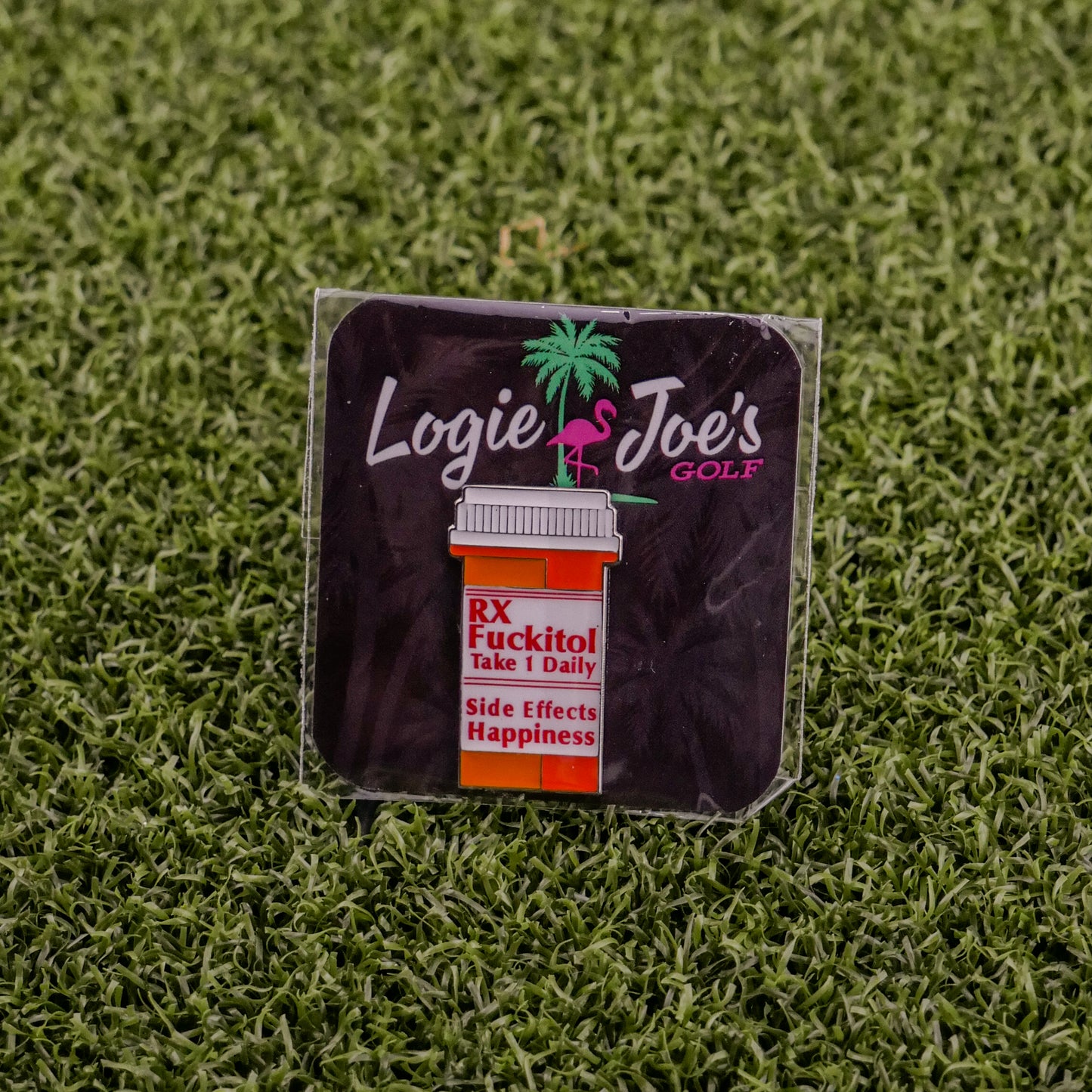 A square sticker on grass displays Ballmarkers by Logie Joe’s RX Fuckitol above a cartoon pill bottle labeled Take 1 Daily. Side effects: happiness, palm tree & flamingo—great for fans of funny golf accessories or unique golf ball markers.
