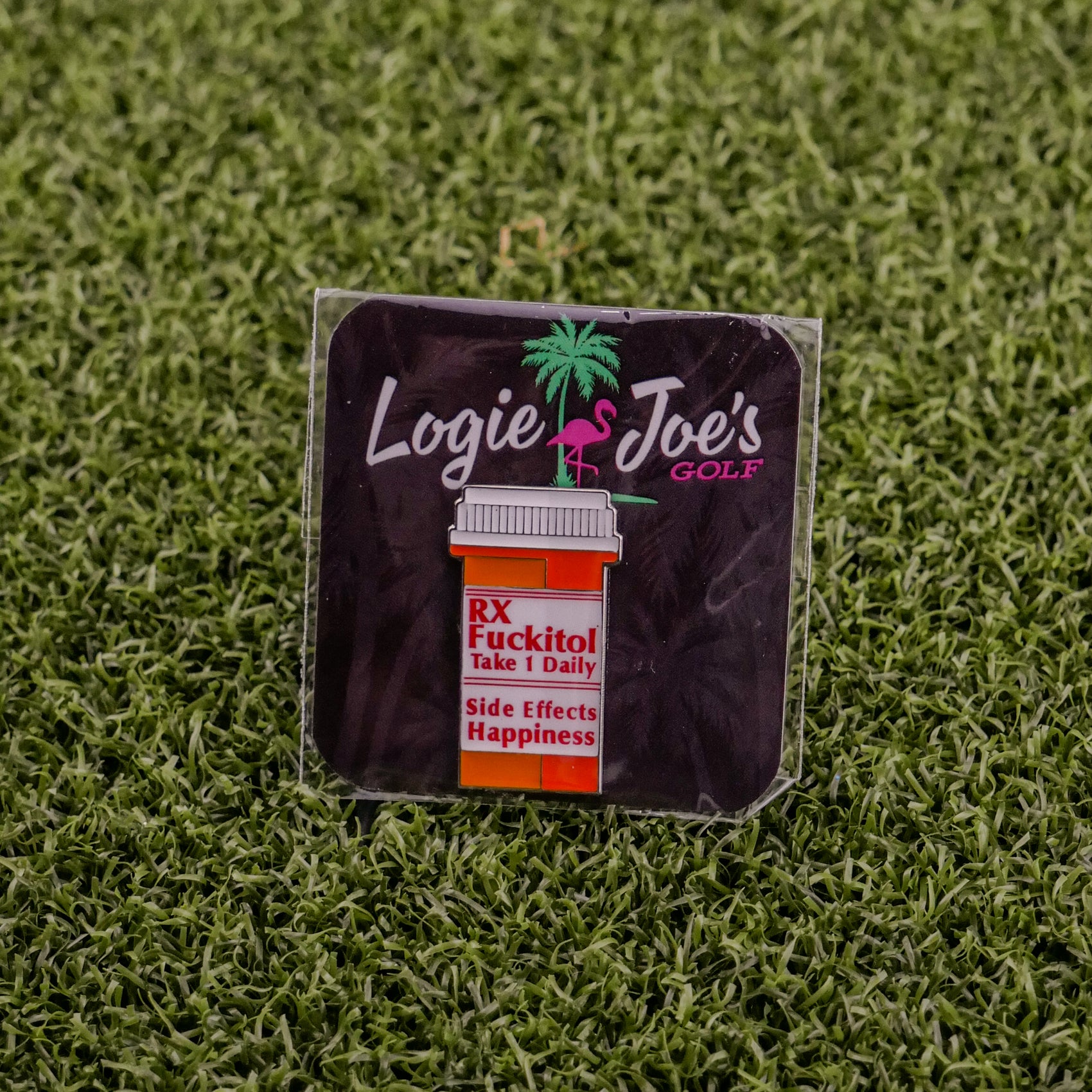 A square sticker on grass displays Ballmarkers by Logie Joe’s RX Fuckitol above a cartoon pill bottle labeled Take 1 Daily. Side effects: happiness, palm tree & flamingo—great for fans of funny golf accessories or unique golf ball markers.
