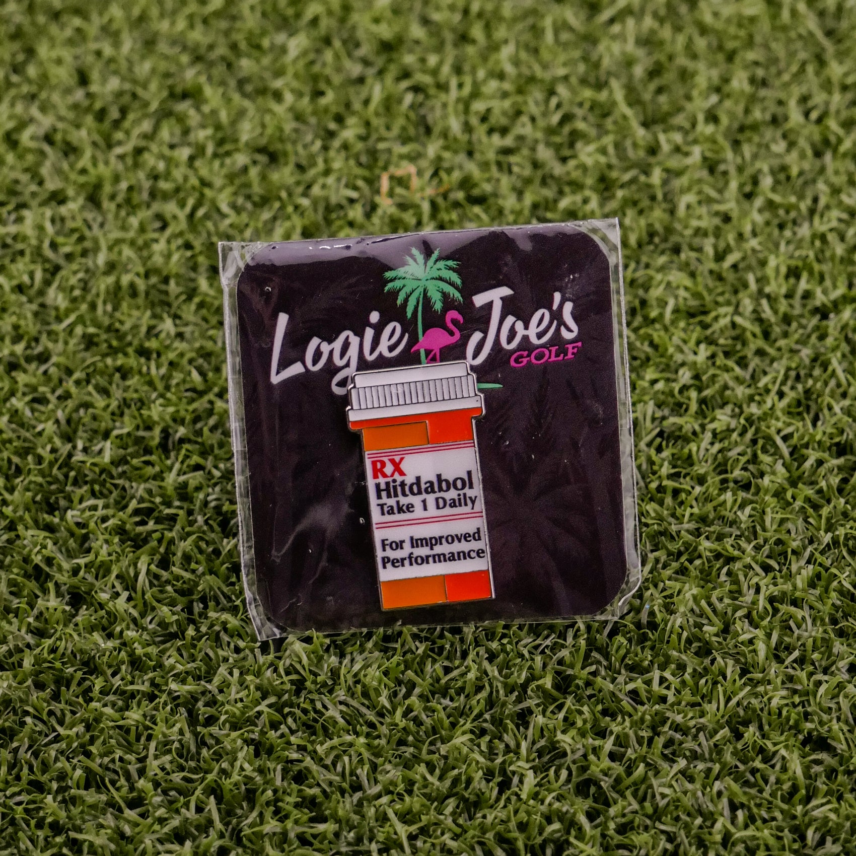 The RX Hitdabol by Ballmarkers from Logie Joe’s is a square golf ball marker styled as a pill bottle, complete with the logo and displayed on green turf—a funny, premium golf accessory for any enthusiast.