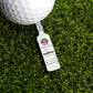 A golf ball rests on artificial grass next to a bottle-shaped metal White Rum Ball Marker from Logie Joe's Golf.