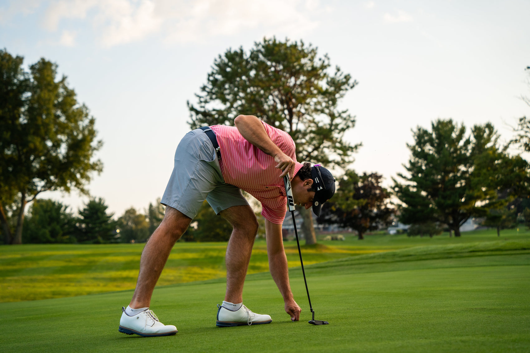 A golfer bends to place a ball on the green, sporting the must-have THE BYRD GOLF DIVOT CLYP by The Byrd, LLC—organize your golf gear before this popular product runs low in stock.
