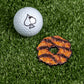 The Pins and Aces Coconut Fudge Cookie Ball Marker, featuring a black spade symbol, rests on artificial grass beside a Samoa-style caramel and coconut cookie.