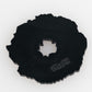 The Coconut Fudge Cookie Ball Marker by Pins and Aces is a black, irregular cast metal marker with a jagged edge, central hole, and matte finish. "PMS & RITE" plus other text are embossed on one side. Shown on a white background.