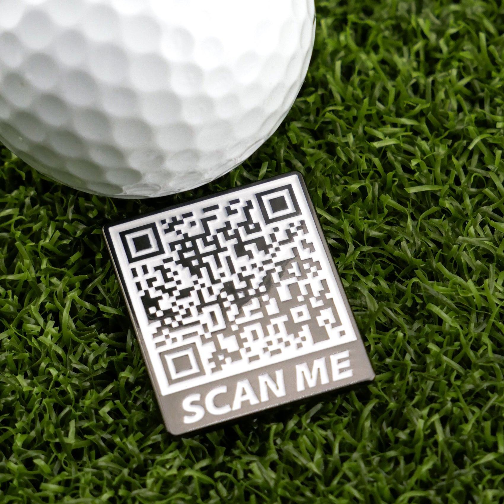 A close-up of Logie Joe's Golf Scan Me—a white golf ball on green grass beside a square QR code labeled "SCAN ME"—showcases unique golf accessories, including a premium ball marker.