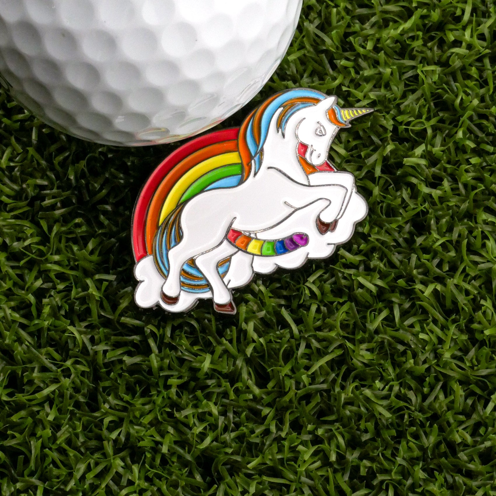 Skittles The Unicorn Ball Marker by Ballmarkers.com features a rainbow-maned unicorn rearing on a cloud with a rainbow, resting on green turf next to a white golf ball—a vibrant and whimsical golf accessory.