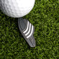 A close-up of a white golf ball on green grass next to the Ballmarkers.com Slide Sandal Ball Marker, a black marker with three white stripes, ready for the putting game.