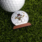 The Frosty the Snow Globe Ball Marker by Ballmarkers.com features a smiling snowman in a black hat and green scarf, sitting on artificial grass next to a white golf ball—perfect for adding festive cheer to your game.