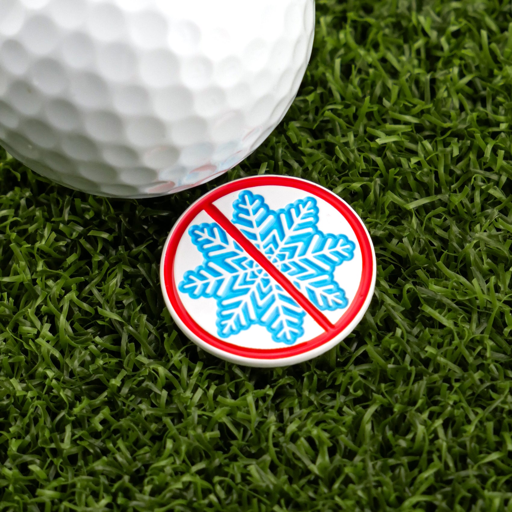 The “Don’t be a Snowflake” golf ball and blue snowflake marker with a red line, by Ballmarkers.com, are displayed on green artificial grass.