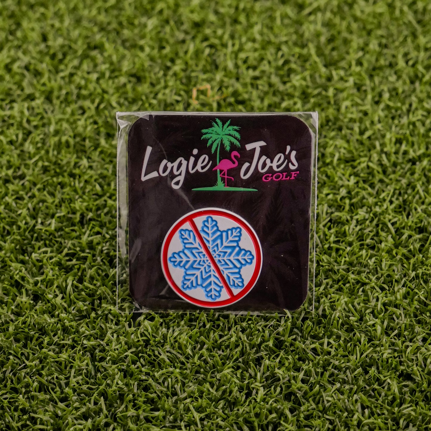 A square badge on artificial grass features Ballmarkers by Logie Joes Don’t be a Snowflake—with a pink flamingo, palm tree, and blue snowflake in a red ban circle—ideal for fans of funny golf accessories or unique golf ball markers.