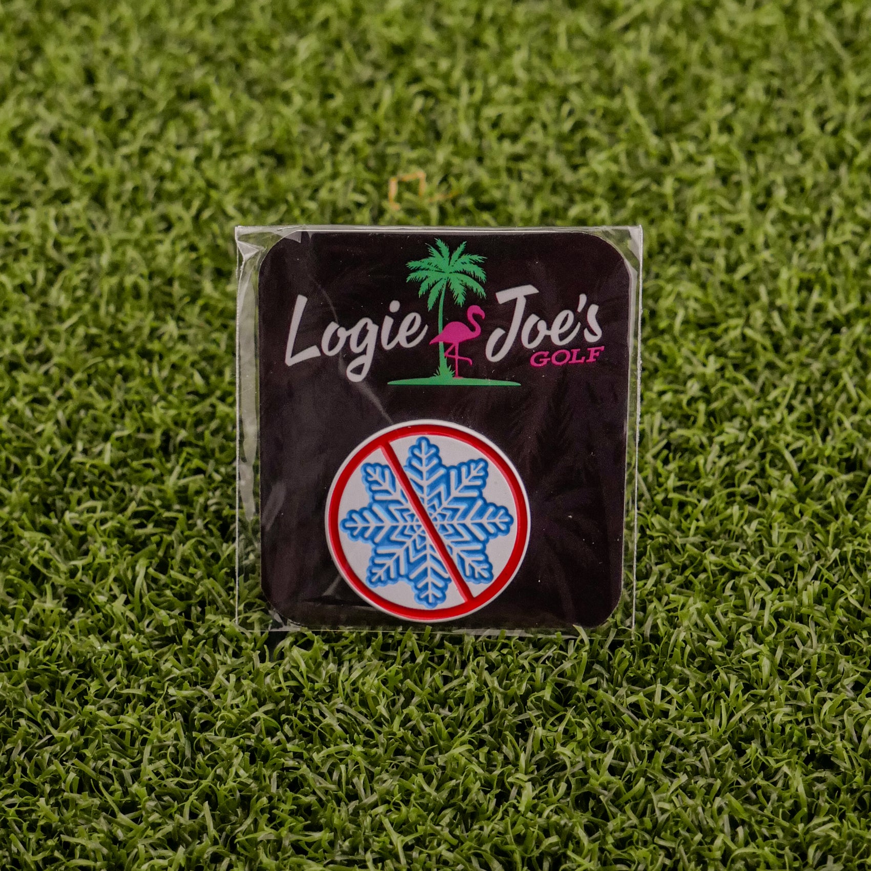 A square badge on artificial grass features Ballmarkers by Logie Joes Don’t be a Snowflake—with a pink flamingo, palm tree, and blue snowflake in a red ban circle—ideal for fans of funny golf accessories or unique golf ball markers.