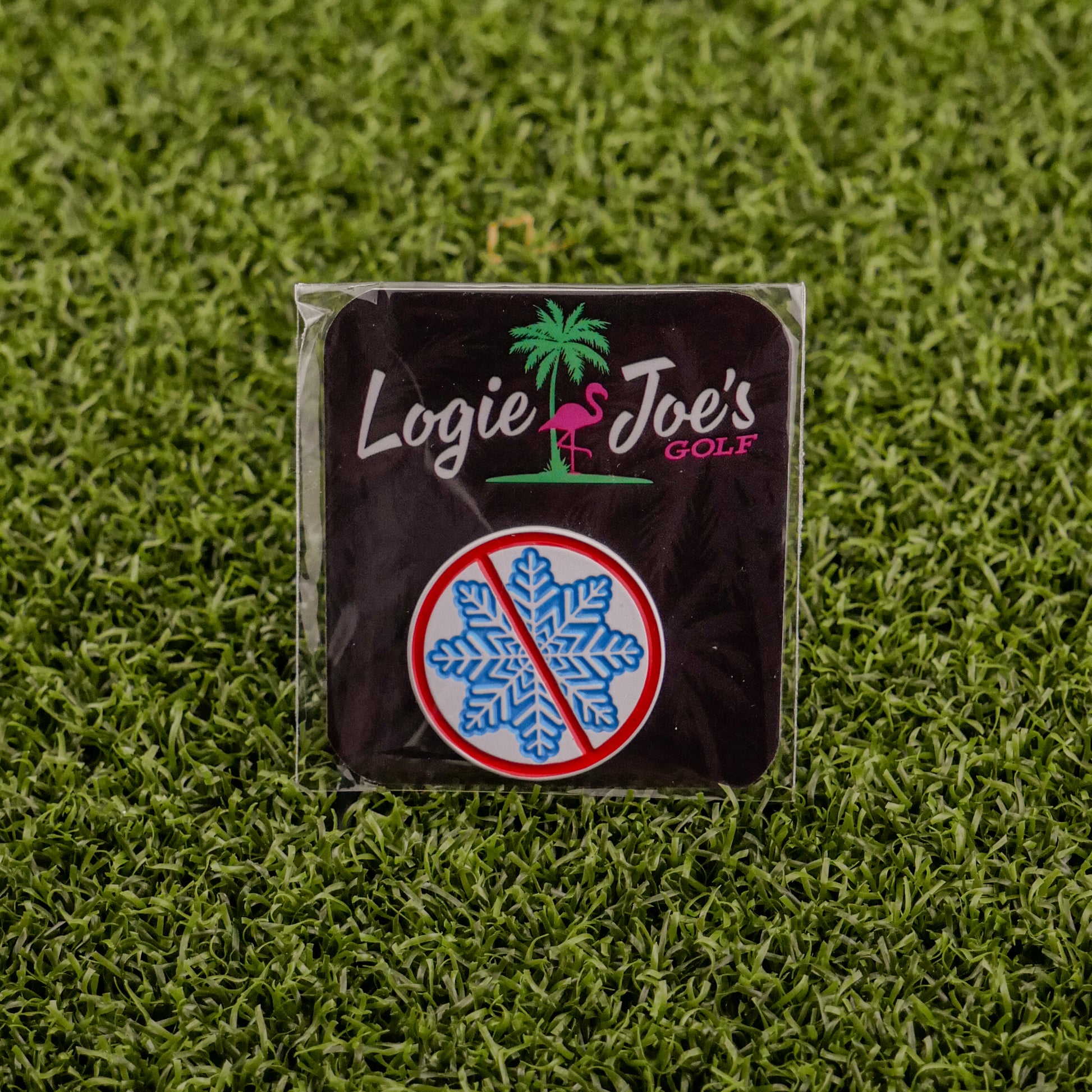 A square badge on artificial grass features Ballmarkers by Logie Joes Don’t be a Snowflake—with a pink flamingo, palm tree, and blue snowflake in a red ban circle—ideal for fans of funny golf accessories or unique golf ball markers.