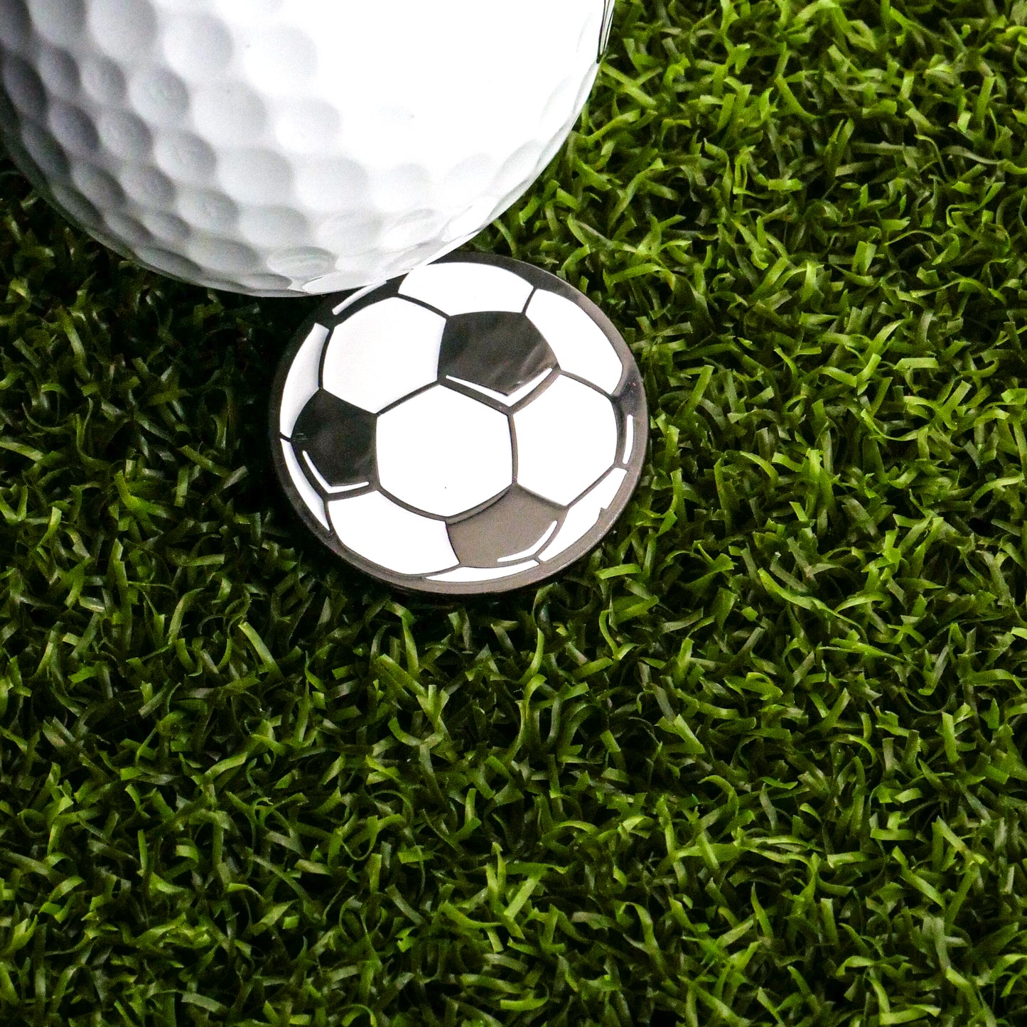 A close-up of a golf ball on artificial green grass with the Ballmarkers.com Soccer Ball Ball Marker emphasizes the precision needed in your short game.