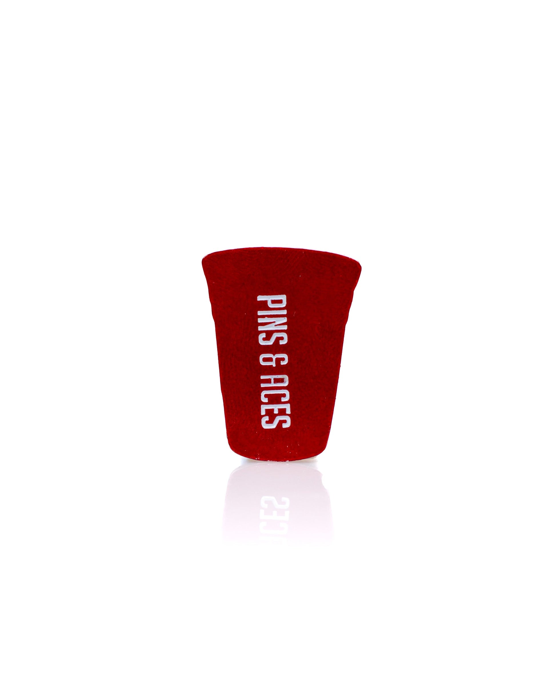 The Red Party Cup Ball Marker by Pins and Aces features "PINS & ACES" printed vertically in white on a red background—a premium golf accessory perfect for any enthusiast.