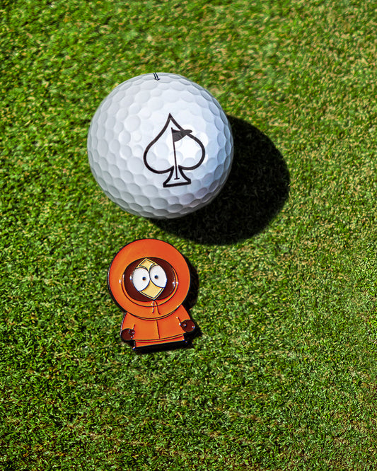 A South Park Ball Marker - Kenny by Pins and Aces, featuring a golf ball with a black spade symbol beside a Kenny figurine in an orange parka, perfect for fans and collectors.