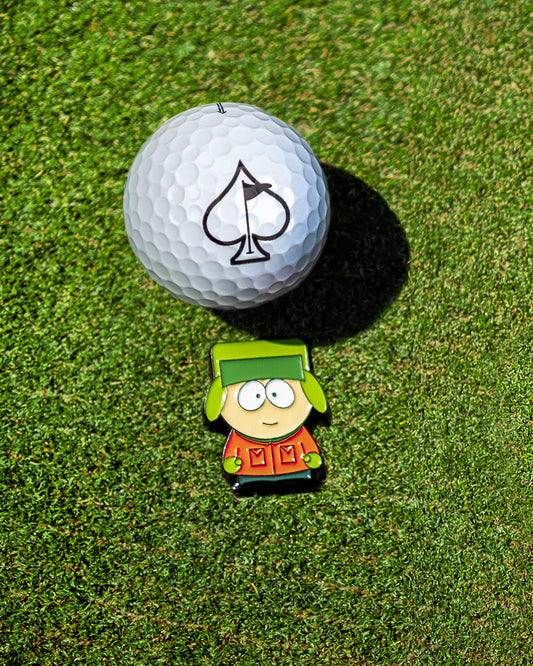 The South Park Ball Marker - Kyle from Pins and Aces features a golf ball with a spade symbol next to a cartoon pin of Kyle in his green hat and orange coat, part of the exclusive South Park collection.