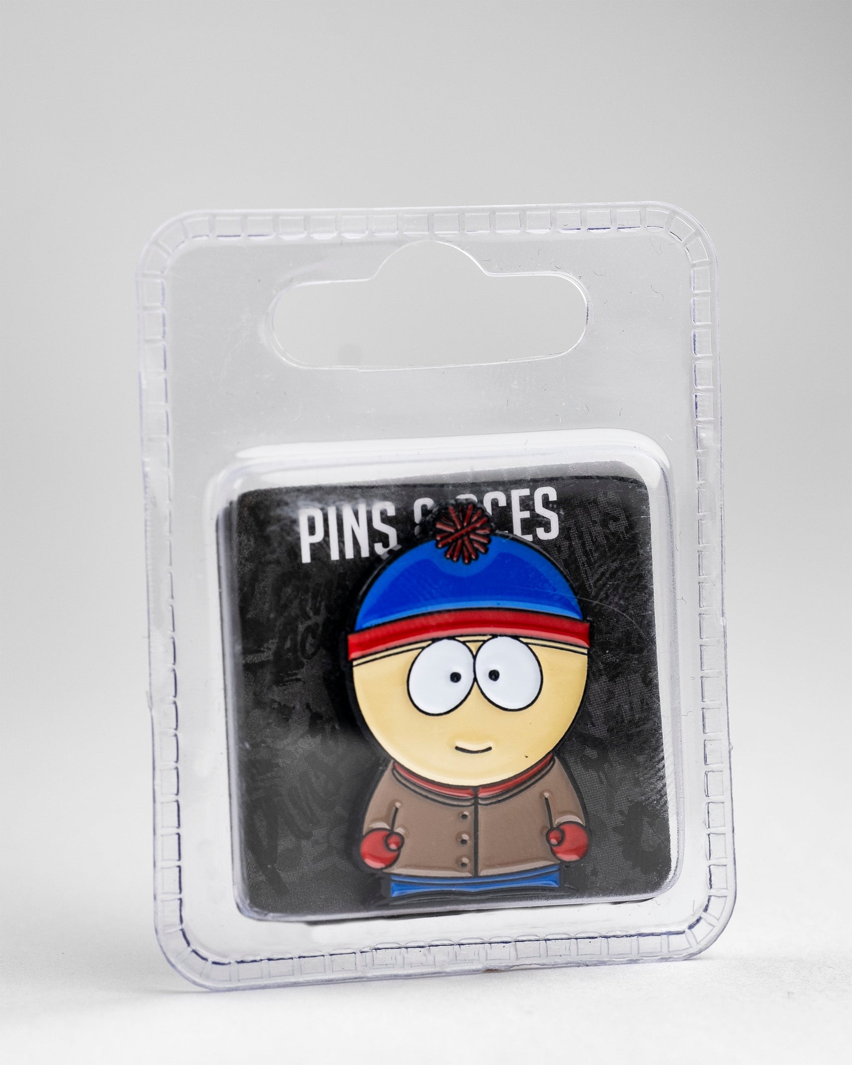 The South Park Ball Marker - Stan by Pins and Aces features Stan in his blue and red hat with a brown jacket, packaged in clear plastic as part of the South Park golf accessories collection.
