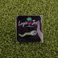 The Sperm Cell pin by Logie Joe's Golf is a playful golf ball marker featuring a cartoon sperm design, displayed on a branded card with a pink flamingo, and set on artificial green grass—ideal for premium golf accessory fans.