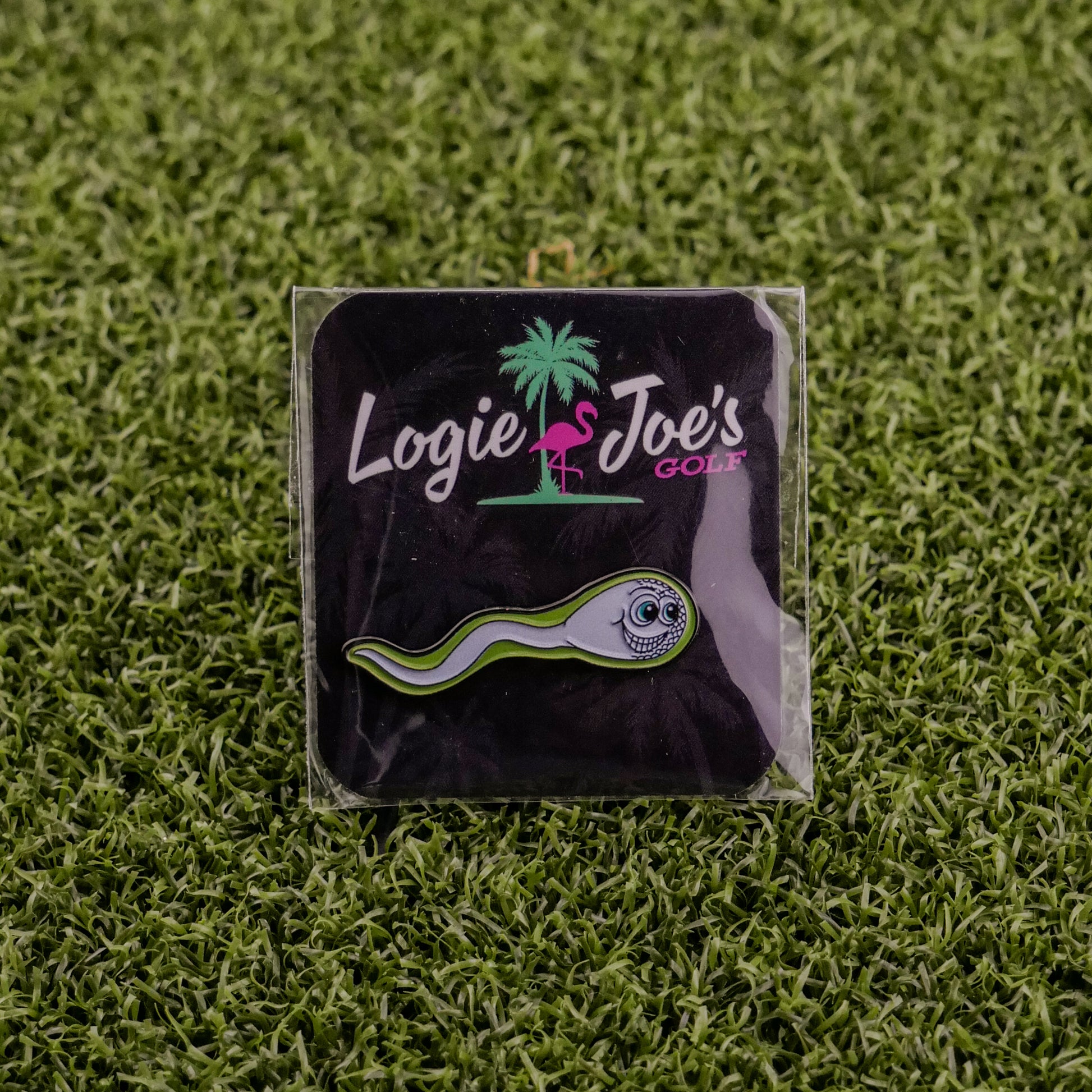 The Sperm Cell pin by Logie Joe's Golf is a playful golf ball marker featuring a cartoon sperm design, displayed on a branded card with a pink flamingo, and set on artificial green grass—ideal for premium golf accessory fans.