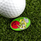 A close-up of a golf ball on artificial grass next to Logie Joe’s Golf "Stinger" marker, featuring a grinning yellow bee with a tee, the word “Stinger,” and a red ball—ideal for fans of premium golf accessories.