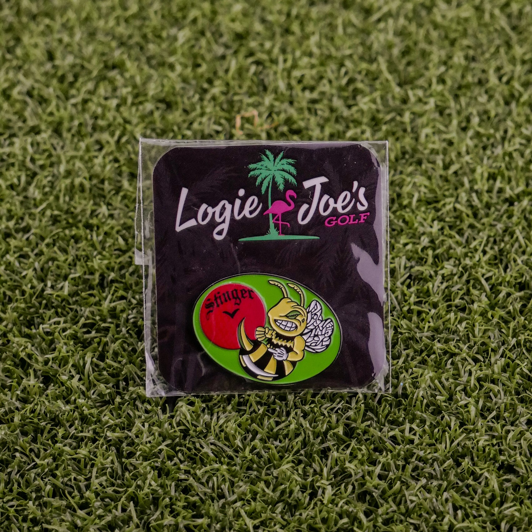 The Logie Joe's Golf Stinger pin set features a bee with a golf club on artificial grass with red, green, and yellow accents. Perfect as premium accessories or unique ball markers for golfers.