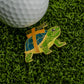 The Strapped Turtle Ball Marker from Logie Joe's Golf, featuring a blue and green shell labeled BANGER, sits on green artificial grass beside a white golf ball.