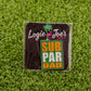 The Sub Par Dad pin by Logie Joe's Golf features green, yellow, and white text and comes on packaging with a pink flamingo and palm tree—an ideal gift for fans of unique golf accessories or personalized ball markers.