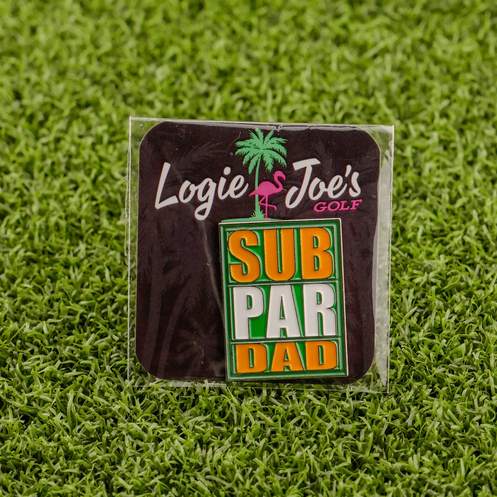 The Sub Par Dad pin by Logie Joe's Golf features green, yellow, and white text and comes on packaging with a pink flamingo and palm tree—an ideal gift for fans of unique golf accessories or personalized ball markers.