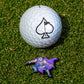 A golf ball with a black spade sits on green grass next to the TMNT - Shredder Ball Marker by Pins and Aces, featuring the cartoon armored villain from Teenage Mutant Ninja Turtles in purple and silver.