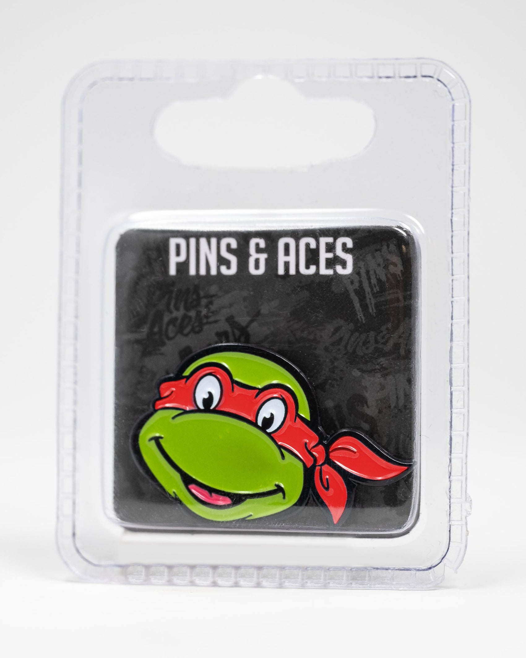 The TMNT - Raphael Ball Marker by Pins and Aces features Raphael’s smiling face, making it a perfect golf accessory. It comes displayed on a black Pins and Aces card and is packaged in a clear plastic case.