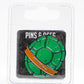 The TMNT - Shell Shock Ball Marker by Pins and Aces features a green enamel turtle shell with an orange band, inspired by Teenage Mutant Ninja Turtles, and comes on a branded card inside clear plastic packaging.