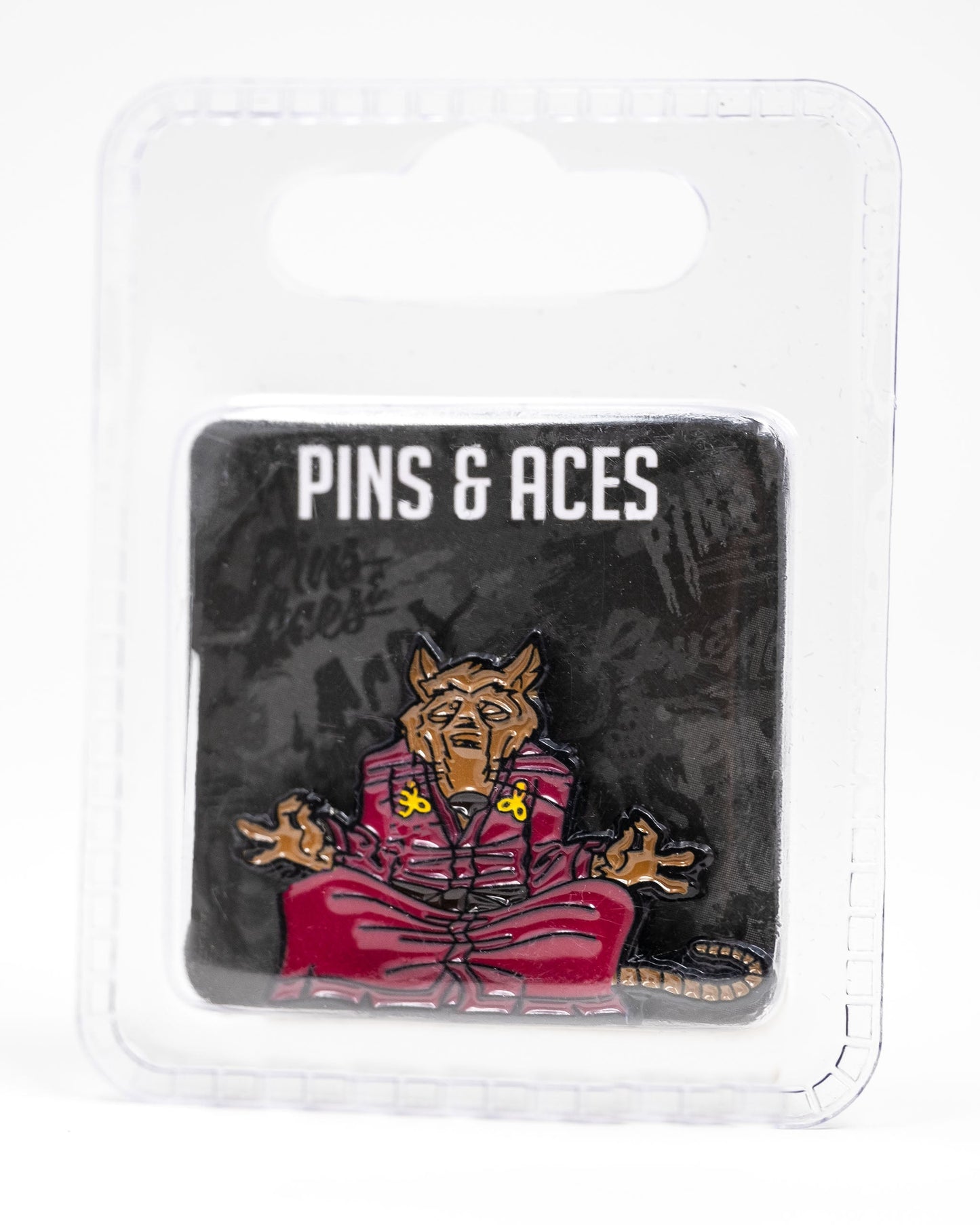 The TMNT - Splinter Ball Marker from Pins and Aces features a meditating brown rat in a red robe, inspired by Splinter. Packaged on a black card with branding in a clear case—perfect for TMNT fans and golf accessory collectors.