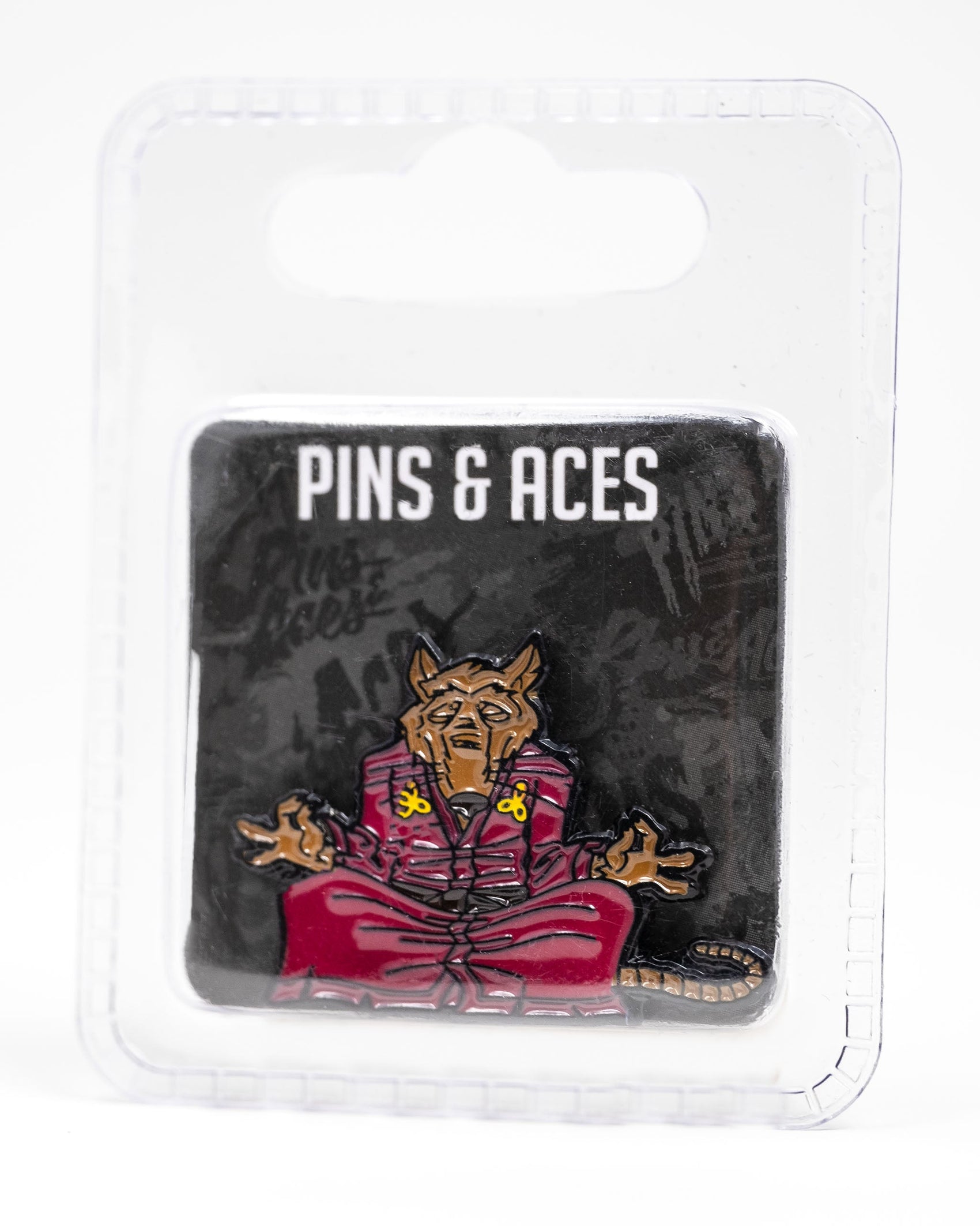 The TMNT - Splinter Ball Marker from Pins and Aces features a meditating brown rat in a red robe, inspired by Splinter. Packaged on a black card with branding in a clear case—perfect for TMNT fans and golf accessory collectors.