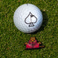 A golf ball with a black spade symbol rests on green grass beside the TMNT - Splinter Ball Marker by Pins and Aces, showcasing a meditating anthropomorphic tiger in red robes—a standout golf accessory.