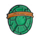 The TMNT - Shell Shock Ball Marker by Pins and Aces features a green turtle shell design with an orange top band, inspired by Teenage Mutant Ninja Turtles, and is shown on a white background with a subtle shadow.