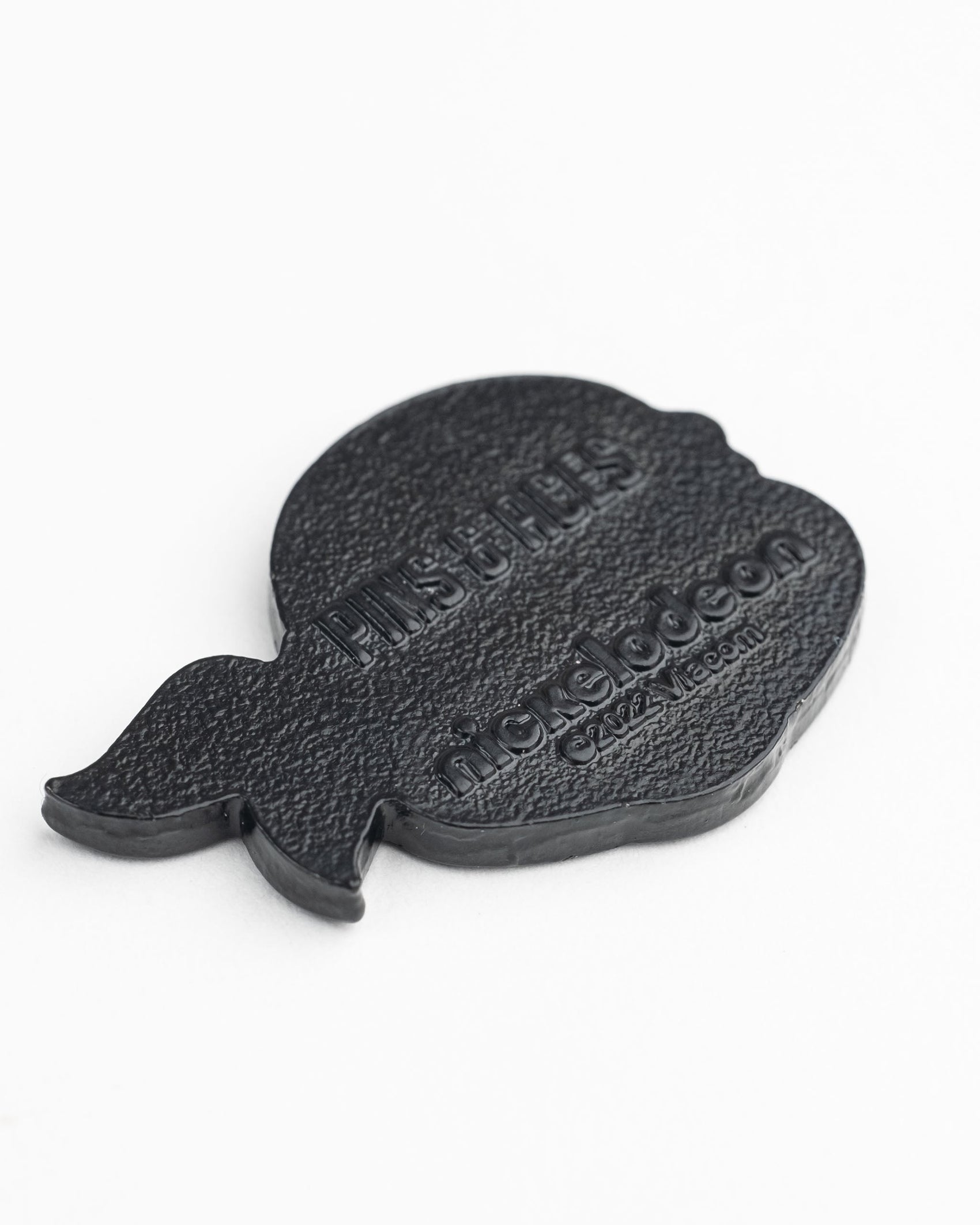 A black head-shaped pin with embossed "PINSUFLIES" and Nickelodeon icons—ideal for Teenage Mutant Ninja Turtles fans. Pair it with your Pins and Aces TMNT - Donatello Ball Marker collection for a unique golf accessory display.