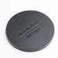 The TMNT - Sewer Cover Ball Marker by Pins and Aces is a round, textured black marker resembling a sewer cover, embossed with Nickelodeon and Pins & Tags, shown on a white background.