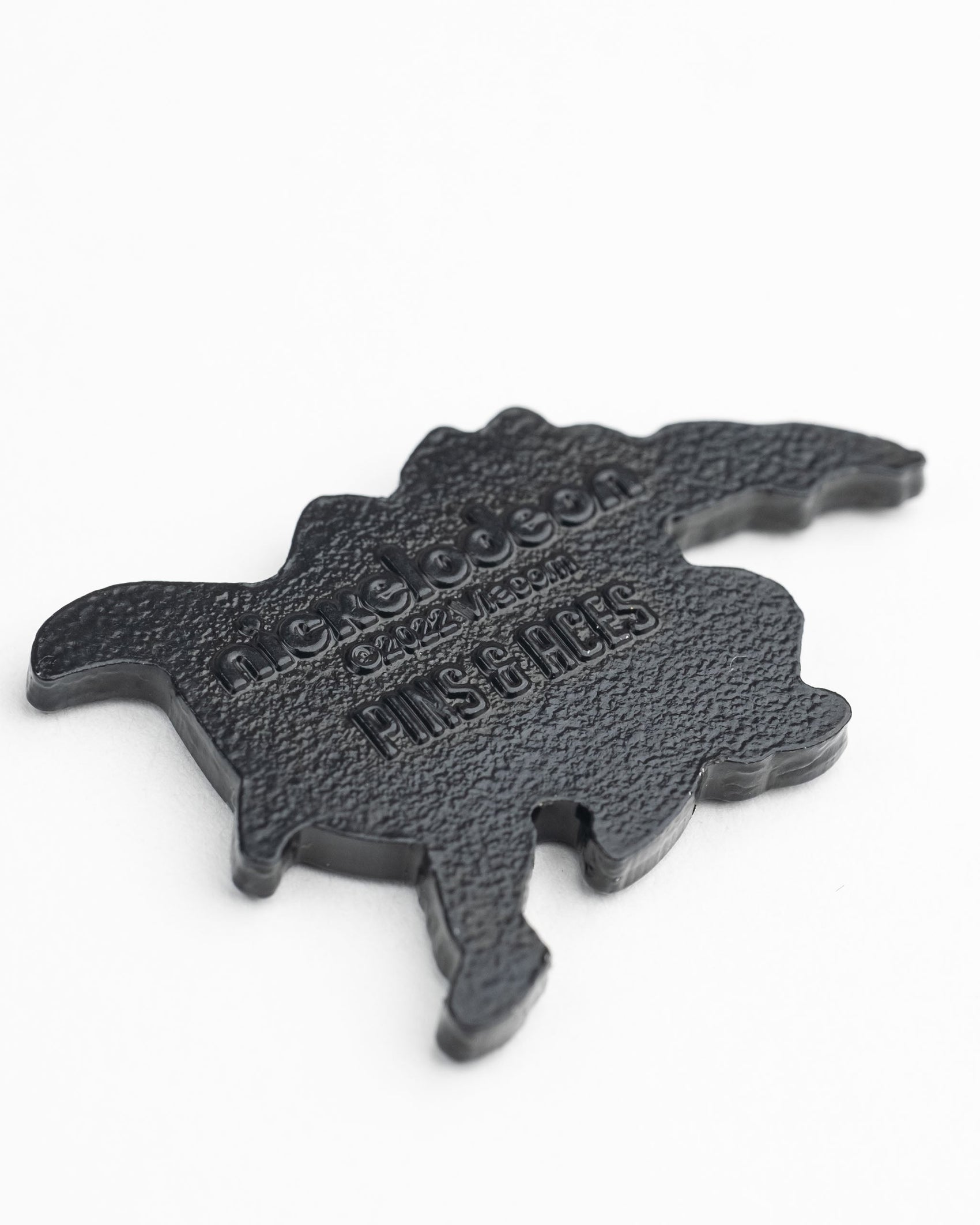 A black plastic TMNT - Shredder Ball Marker by Pins and Aces, turtle-shaped with raised “nextdoossn” and “PLUS OF AGES” text, resembling a Teenage Mutant Ninja Turtles golf accessory, shown on a white background.